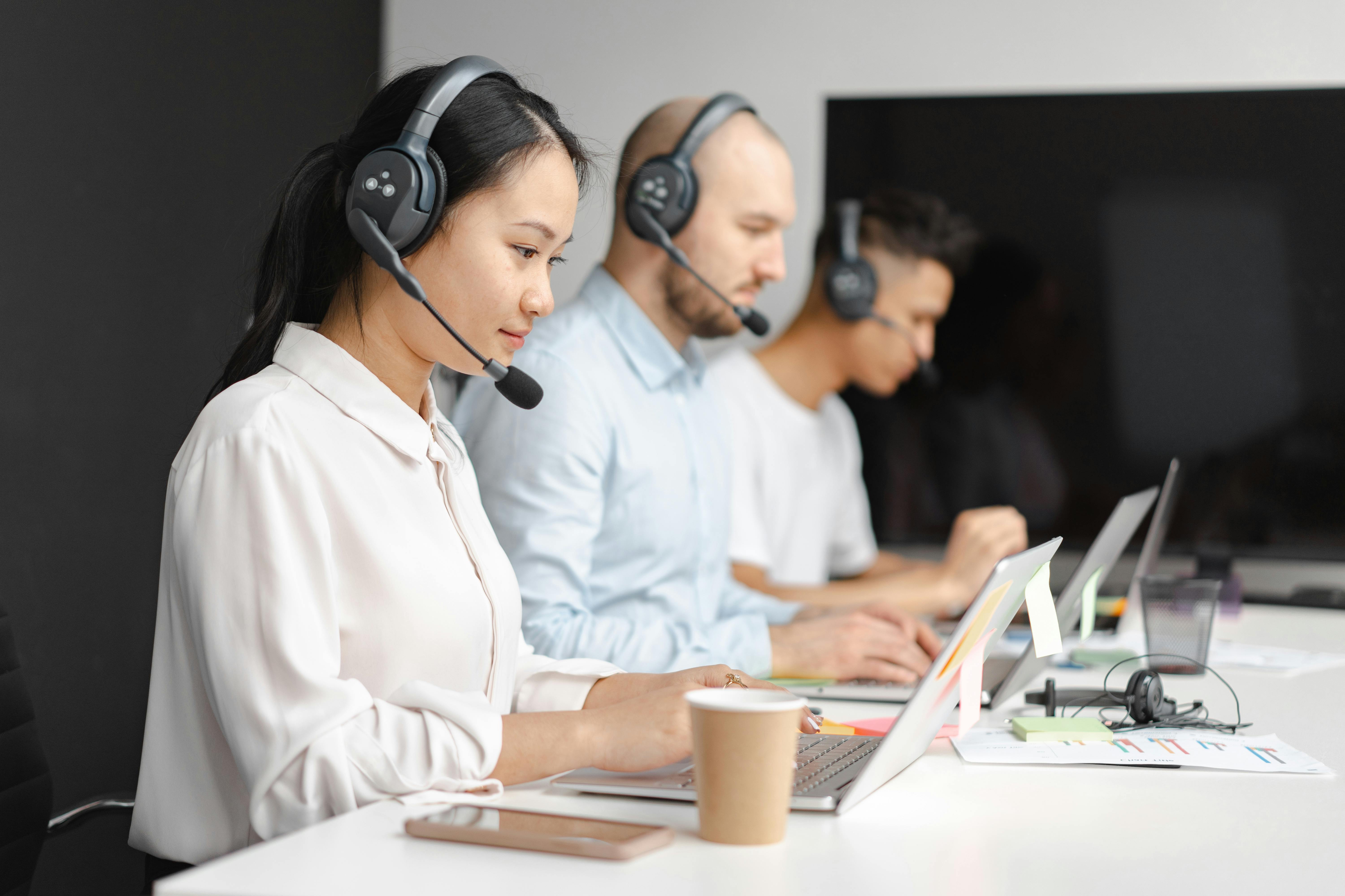 People sitting at a desk working on laptops with a headset on