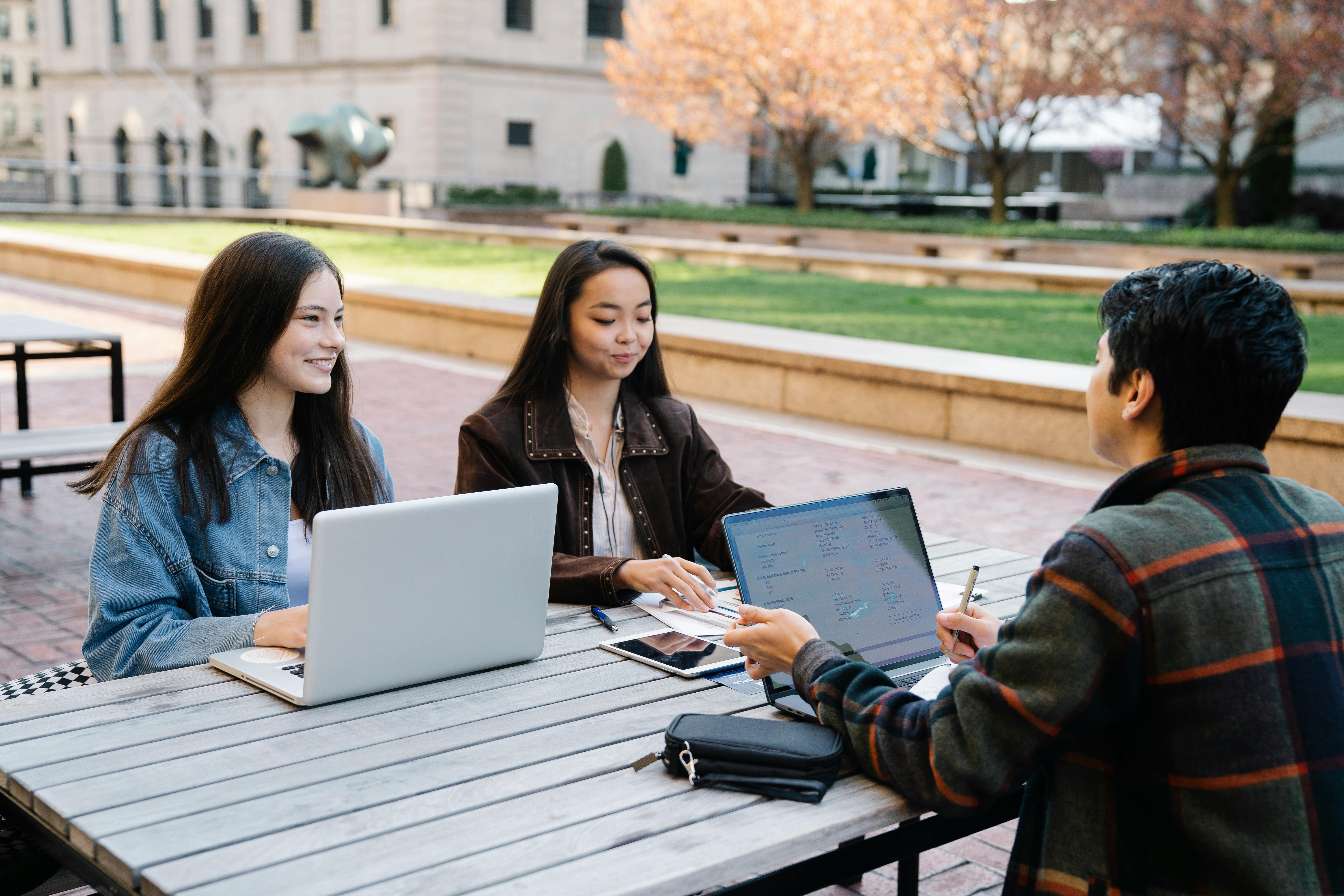 Three Young People Studying Together Outdoors With Laptops