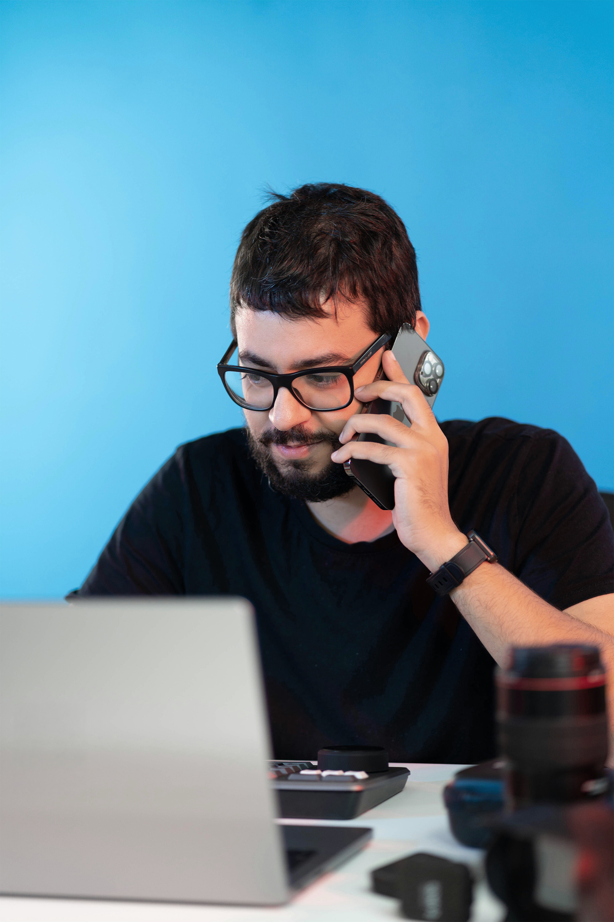 Man sitting at a desk looking at a laptop while talking on a mobile phone