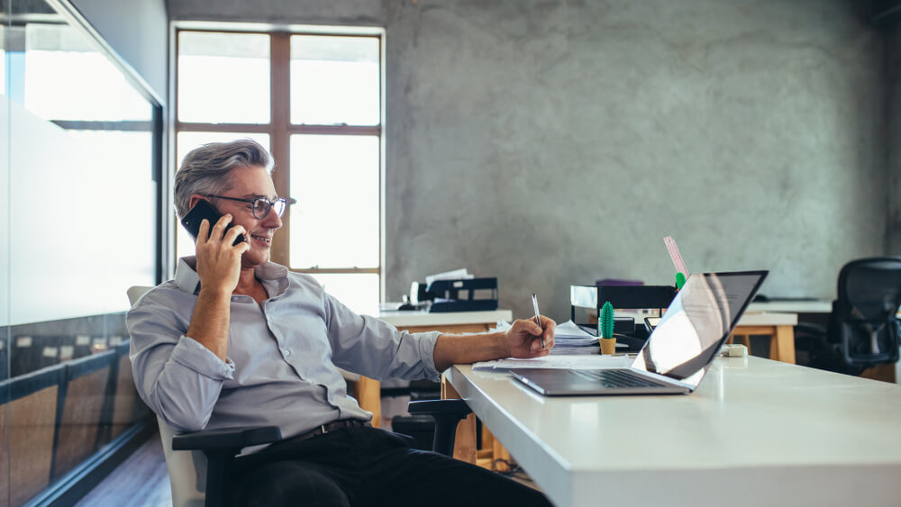 Small business owner at his desk talking on his phone while working online.