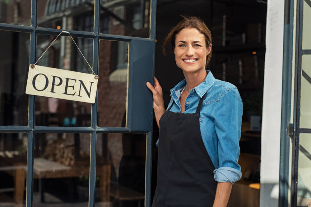 Shop owner standing in doorway with open sign, supported by Business NBN.