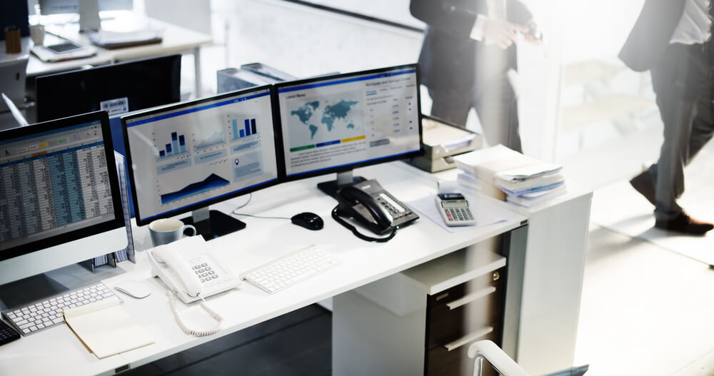 Office desk with multiple monitors displaying business data, supported by fast Business NBN.