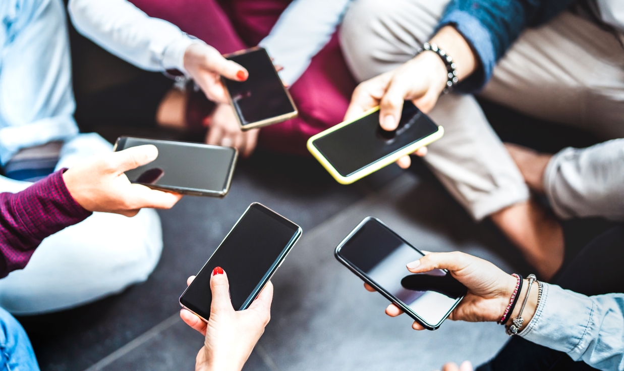 Group of people sitting in a circle holding up their phones together in the middle of the circle