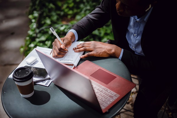 Man on laptop while writing on notepad
