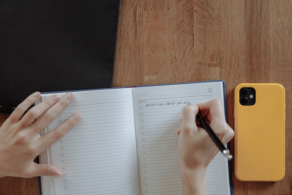 Person Writing in Journal with Phone by the Side